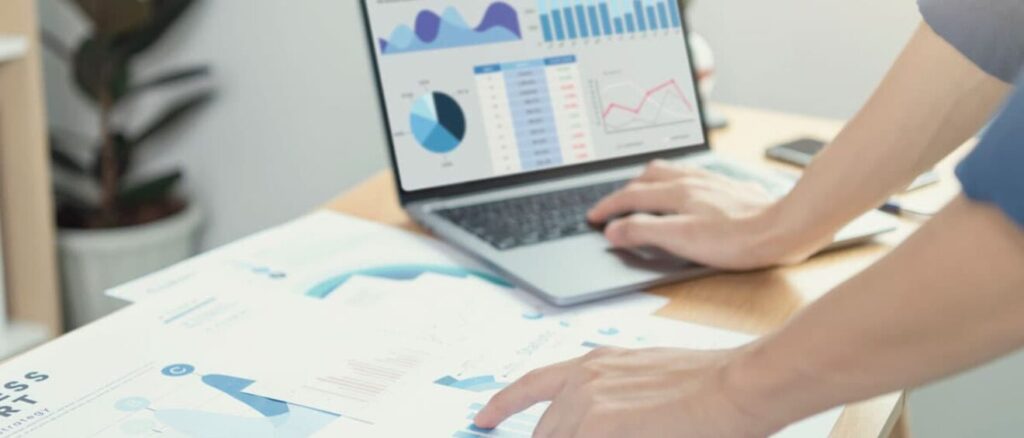 A person analyzes data on a laptop, surrounded by printed graphs and charts, in a modern office setting.