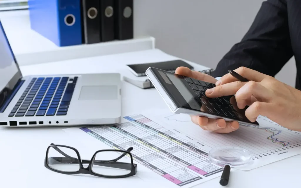 A businessman holding a calculator With his laptop and glasses in his desk