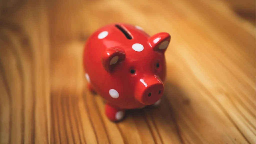 A red piggy bank with white polka dots sits on a wooden table, ready to collect coins.