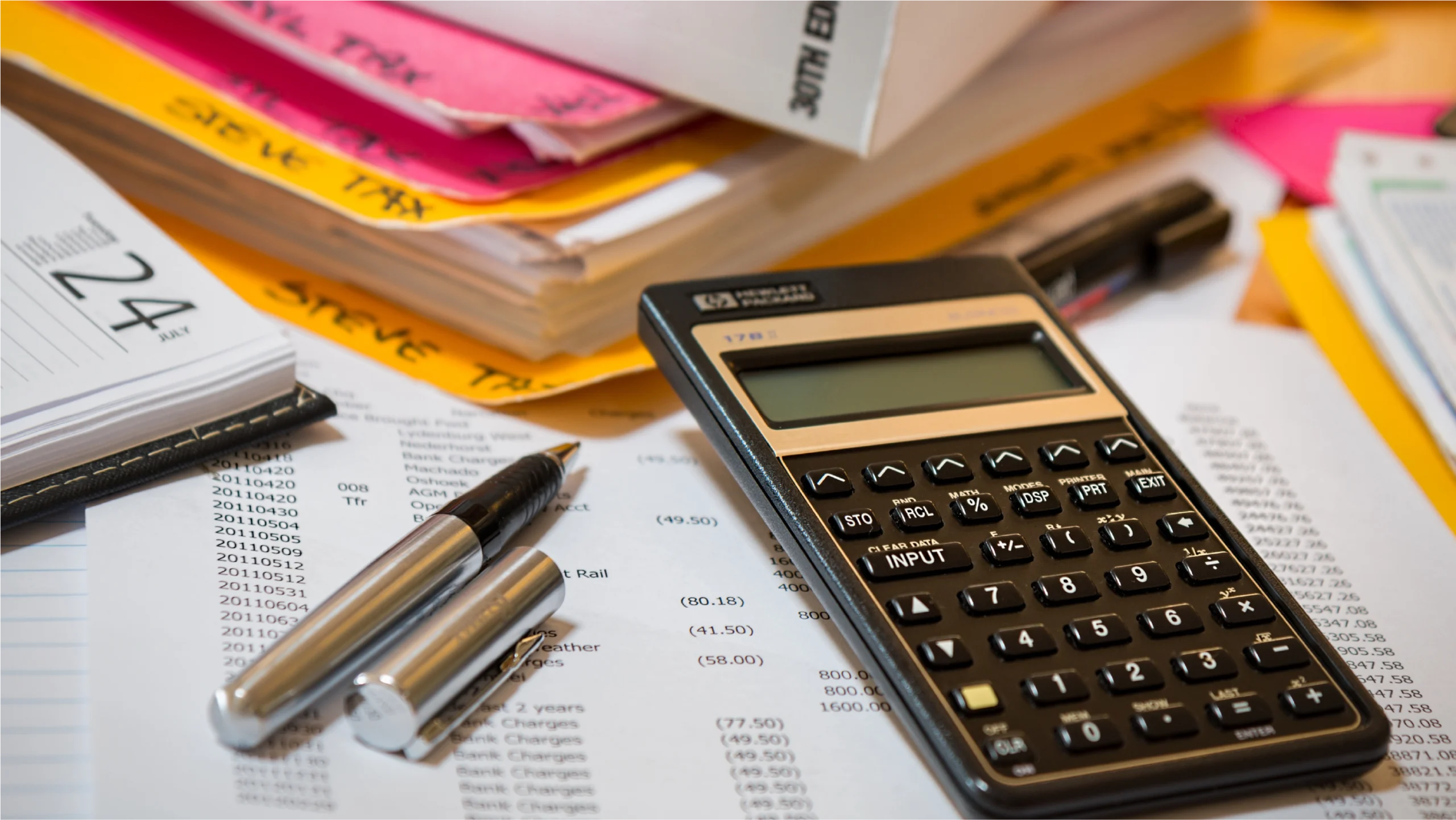 A close-up of a calculator, pens, and scattered financial documents, including a calendar