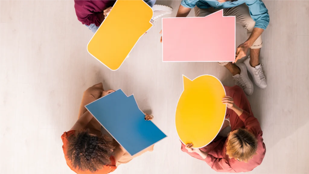 Top view of five people holding colorful speech bubbles, suggesting a group discussion or conversation.