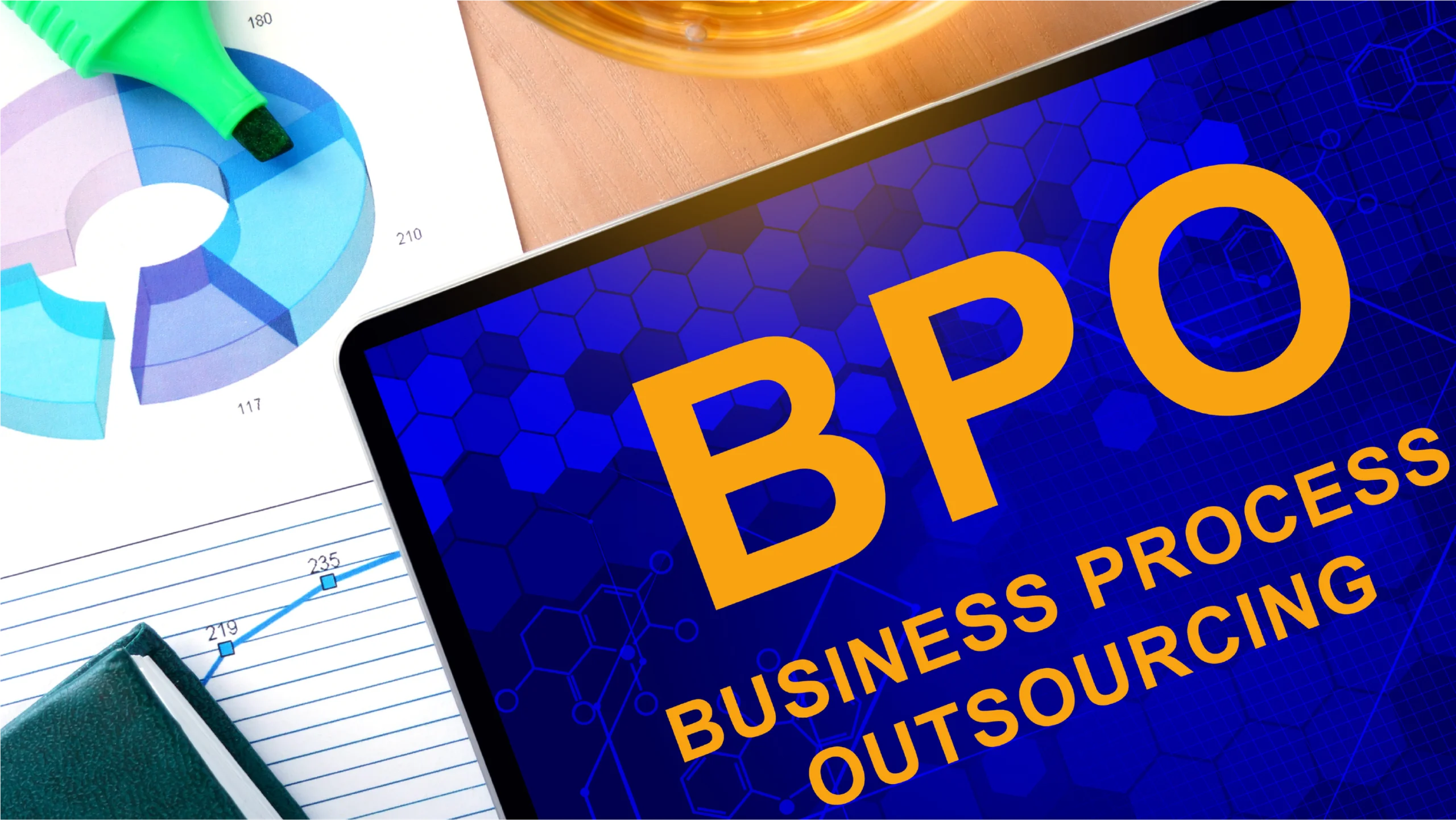 A tablet displaying "BPO BUSINESS PROCESS OUTSOURCING" beside colorful charts and a green highlighter on a wooden desk.