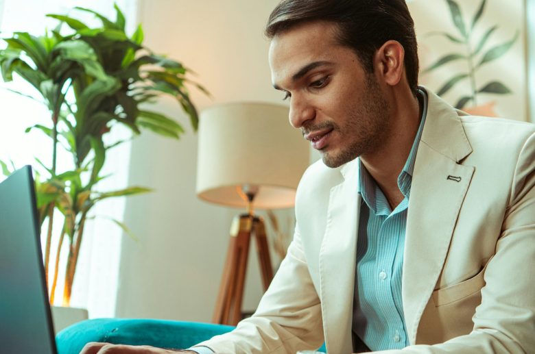 Man in a blazer typing on a laptop