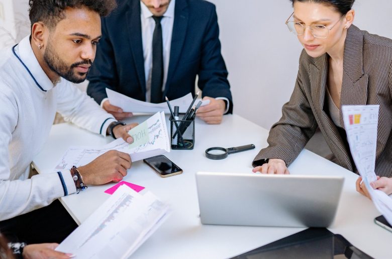 Three colleagues reviewing papers around a laptop