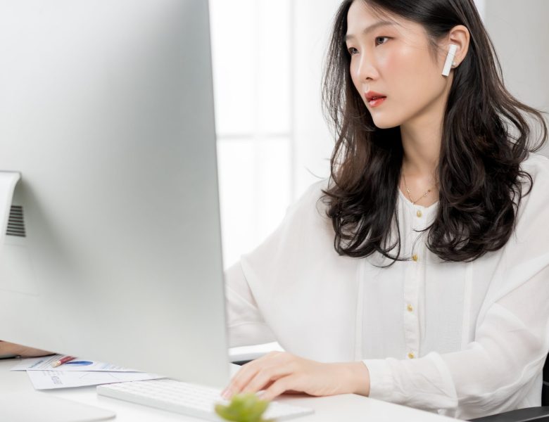 Woman wearing earbuds working at a desktop computer