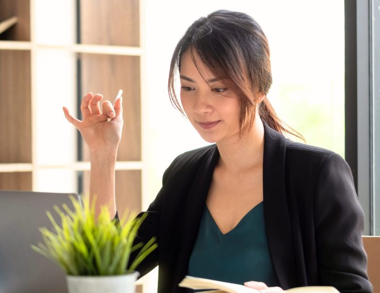 Woman in a blazer gesturing while reading at her desk