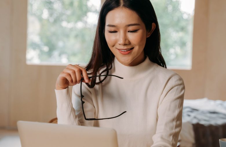 Smiling woman holding her glasses in front of a laptop