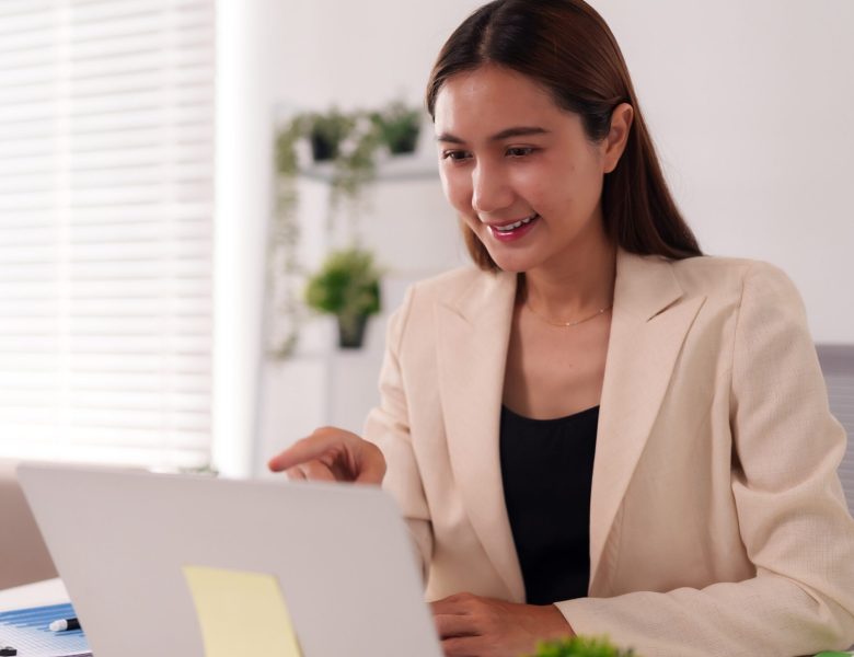 Smiling woman in a blazer working on a laptop