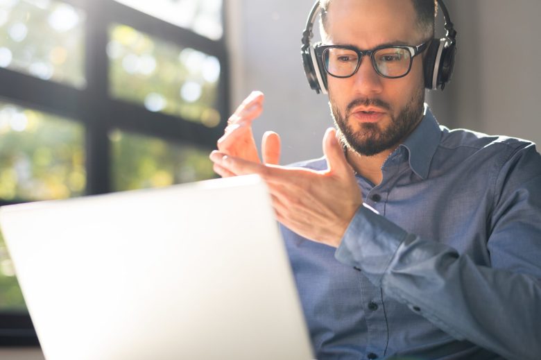 Man wearing headphones talking and gesturing at his laptop