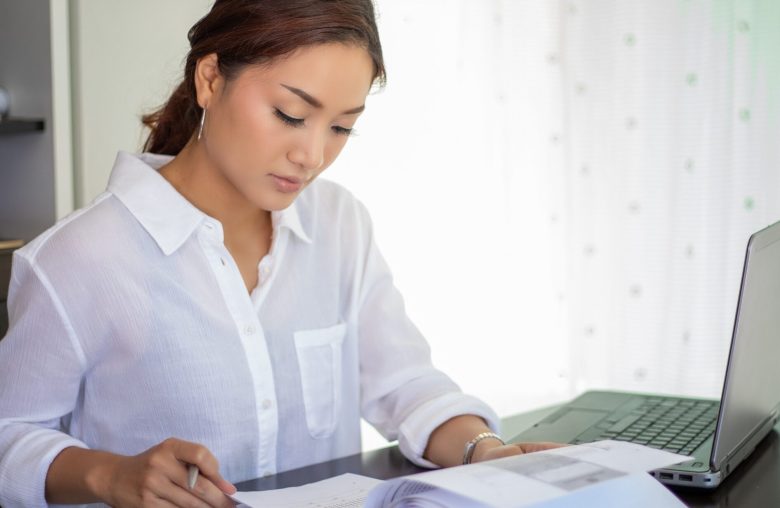 Woman writing notes at a desk beside a laptop