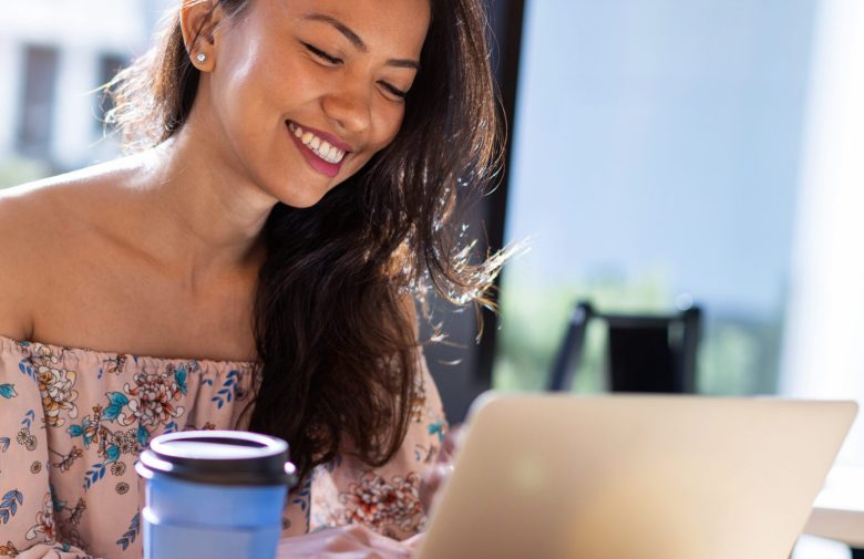 Smiling woman working on a laptop with a coffee cup