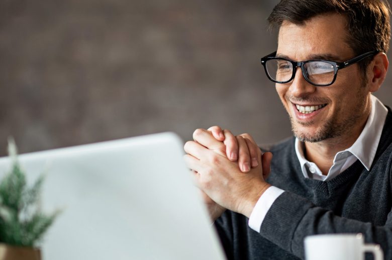 Smiling man in glasses sitting at a laptop