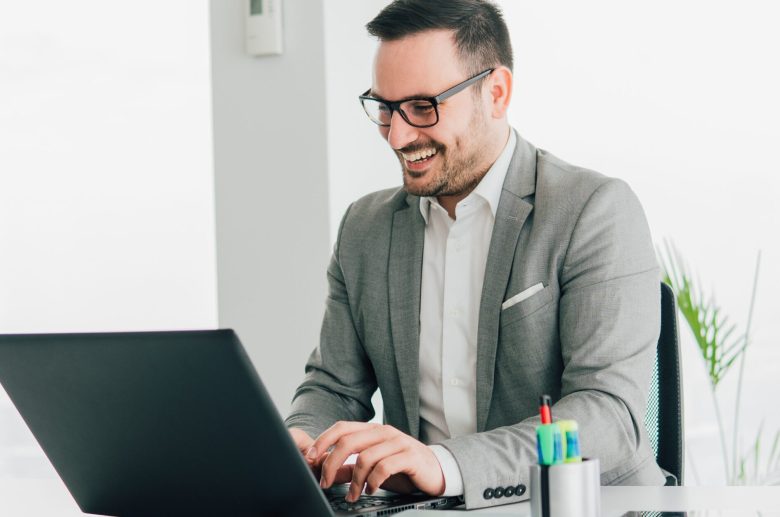 Smiling man in glasses typing on a laptop