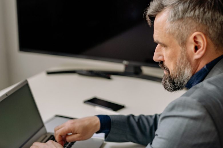 Man working on a laptop at a desk with a large monitor