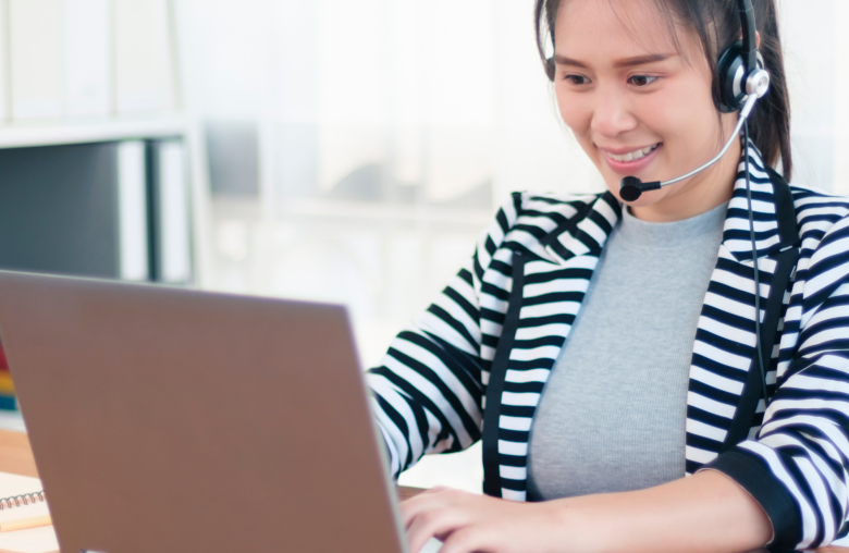 Smiling woman wearing a headset typing on a laptop