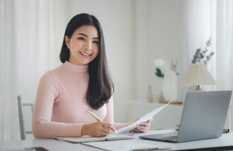 Smiling woman writing notes at a desk with a laptop