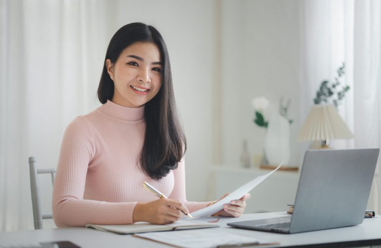 Smiling woman writing notes at a desk with a laptop