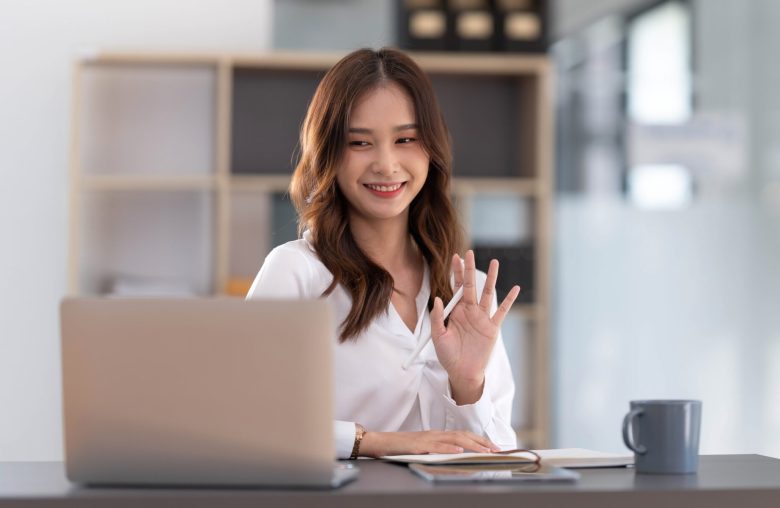 Smiling woman waving at her laptop during a video call