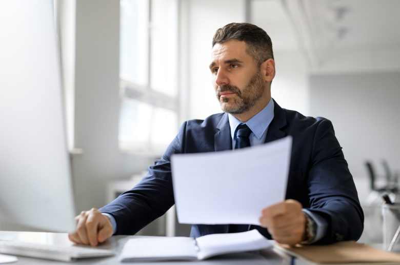 Man in a suit reading a document at his desk