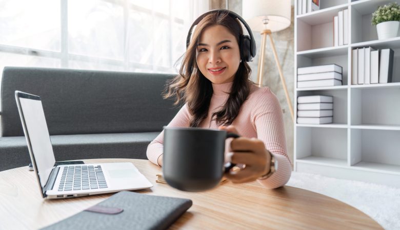 Smiling woman wearing headphones holding a mug at her desk