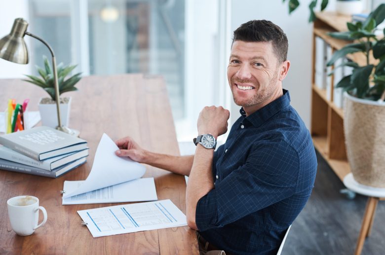 Smiling man at a desk with papers and a coffee cup