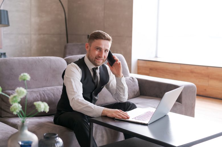 Man on the phone sitting on a sofa with a laptop