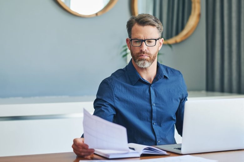 Man in glasses reading a document at his laptop