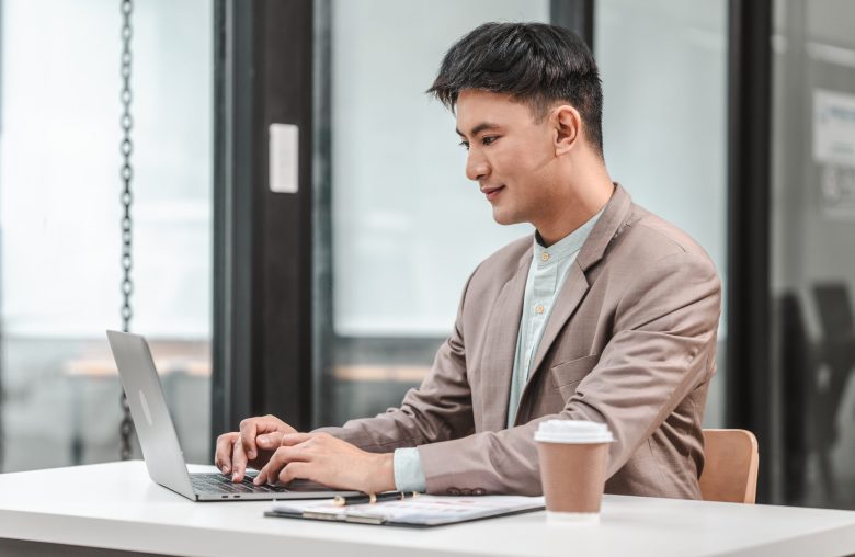 Man in a blazer typing on a laptop