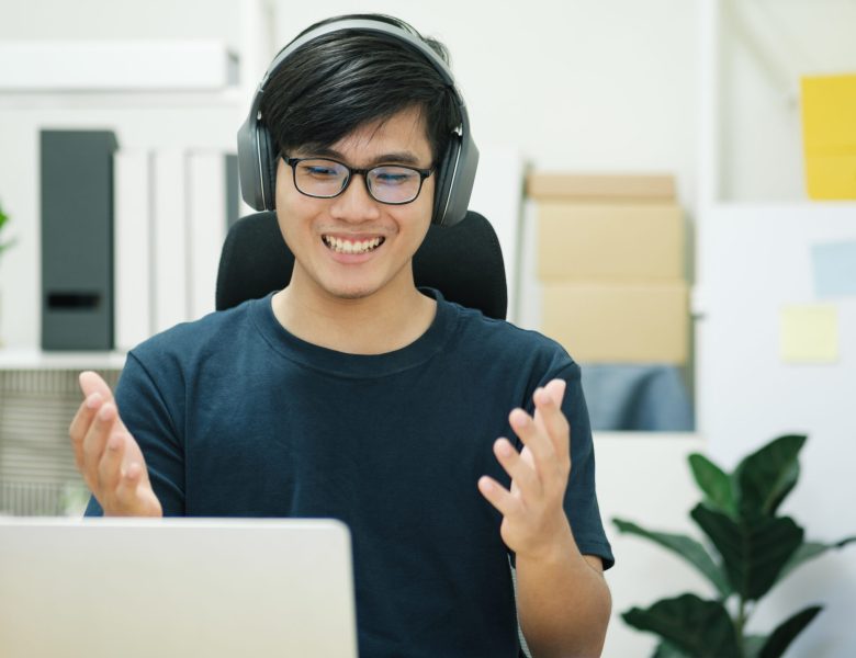 Smiling man wearing headphones talking at his laptop